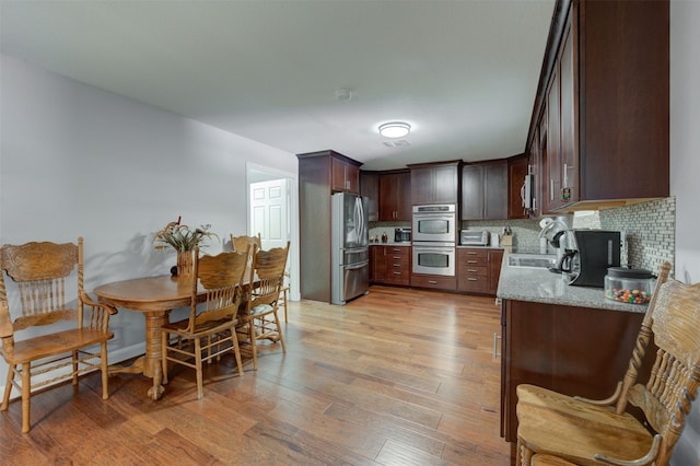 kitchen featuring appliances with stainless steel finishes, light wood-type flooring, tasteful backsplash, dark brown cabinets, and sink