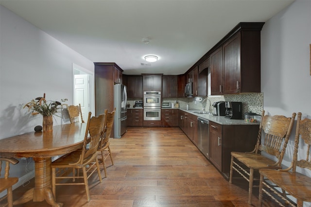 kitchen with decorative backsplash, light wood-type flooring, dark brown cabinets, stainless steel appliances, and sink