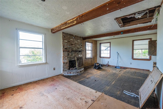 unfurnished living room featuring beamed ceiling, a textured ceiling, hardwood / wood-style flooring, and a brick fireplace