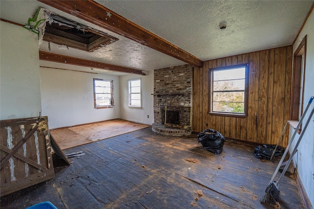 unfurnished living room with beamed ceiling, a textured ceiling, wooden walls, and a brick fireplace