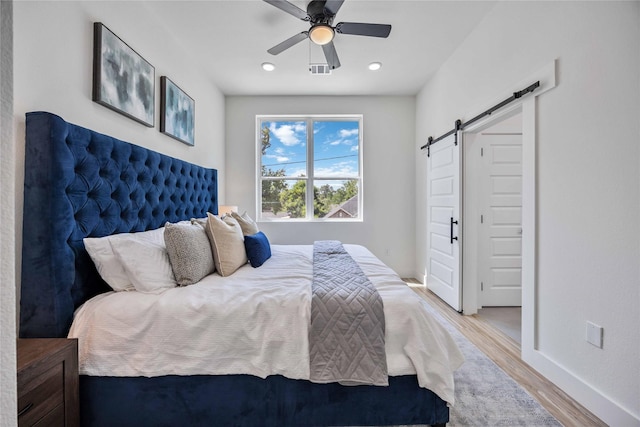 bedroom featuring hardwood / wood-style flooring, ceiling fan, and a barn door