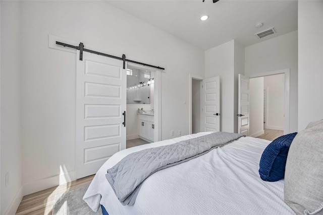 bedroom with connected bathroom, light hardwood / wood-style flooring, and a barn door