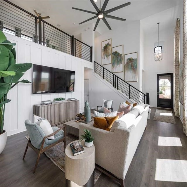 living room featuring a high ceiling, ceiling fan with notable chandelier, and dark wood-type flooring