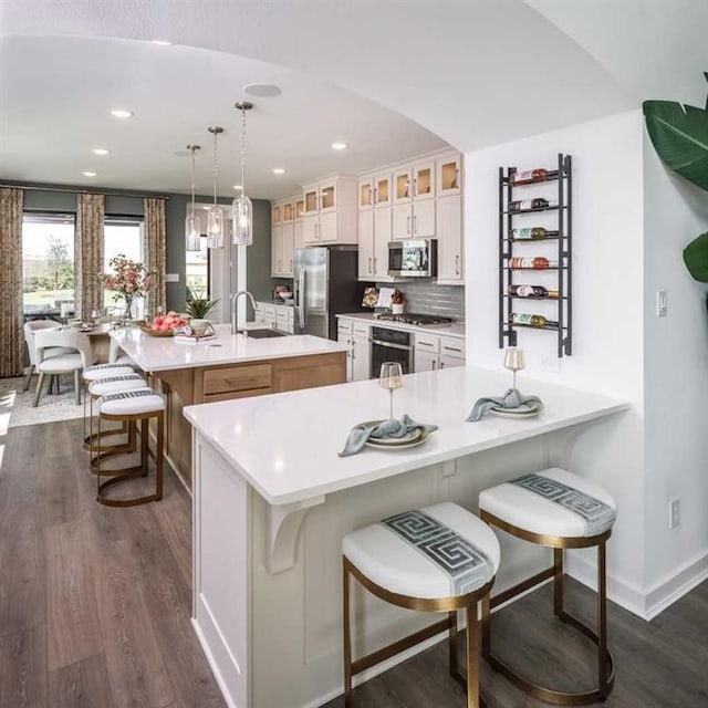 kitchen with an island with sink, appliances with stainless steel finishes, decorative light fixtures, a kitchen bar, and white cabinetry