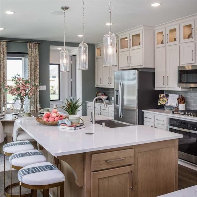 kitchen with a large island, sink, backsplash, white cabinets, and appliances with stainless steel finishes