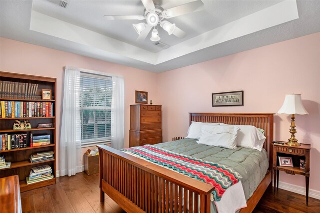 bedroom featuring a tray ceiling, ceiling fan, and dark wood-type flooring