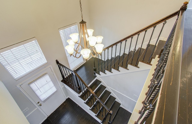 stairway featuring a towering ceiling, hardwood / wood-style flooring, and an inviting chandelier