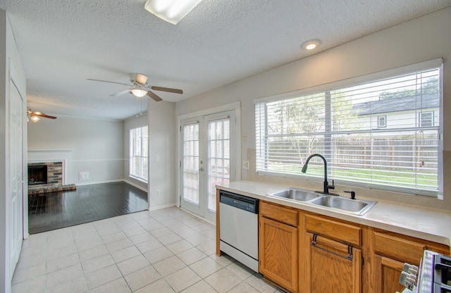 kitchen with ceiling fan, dishwasher, sink, a brick fireplace, and light hardwood / wood-style floors