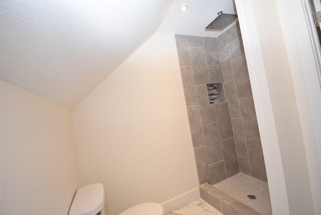 bathroom with a tile shower, vaulted ceiling, and toilet