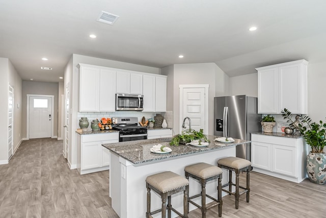 kitchen with white cabinets, sink, light hardwood / wood-style flooring, an island with sink, and stainless steel appliances