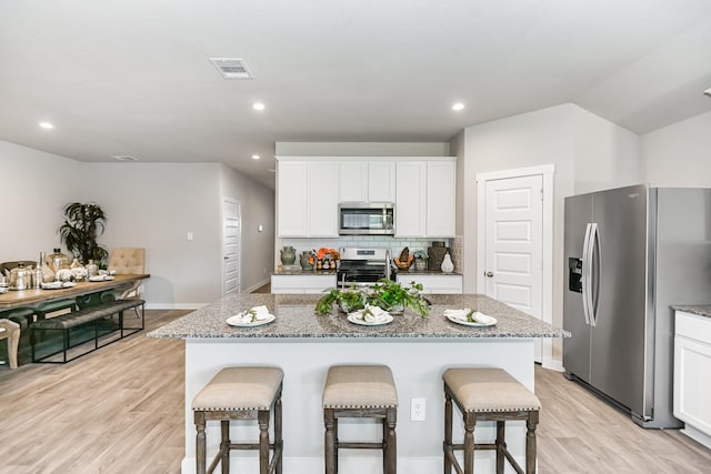 kitchen with white cabinets, stainless steel appliances, light hardwood / wood-style flooring, and an island with sink