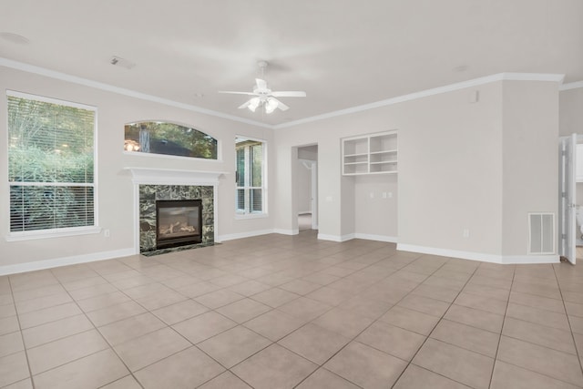 unfurnished living room featuring ceiling fan, ornamental molding, light tile patterned floors, and a tiled fireplace