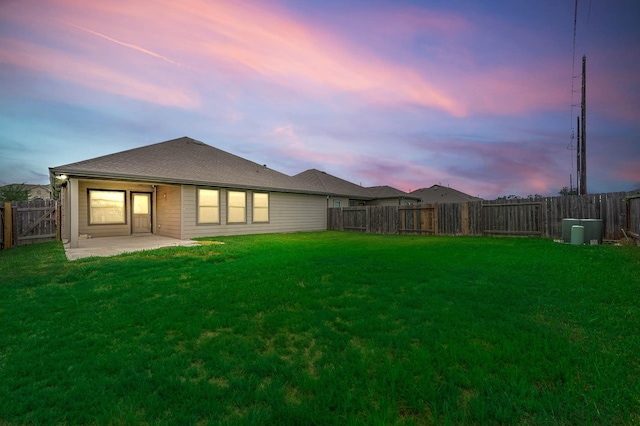 back house at dusk with a lawn and a patio area