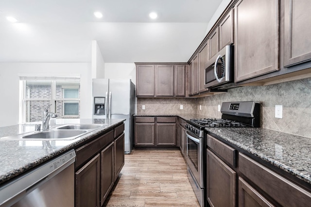 kitchen featuring dark brown cabinetry, sink, light stone counters, appliances with stainless steel finishes, and light wood-type flooring