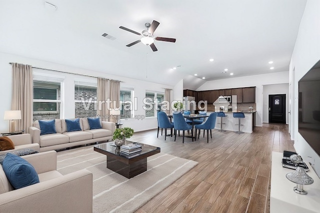 living room with ceiling fan, light hardwood / wood-style floors, and vaulted ceiling