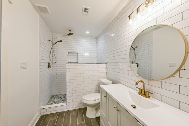 bathroom featuring toilet, a tile shower, tile walls, and vanity