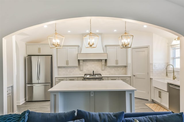 kitchen with tasteful backsplash, custom exhaust hood, stainless steel appliances, sink, and decorative light fixtures