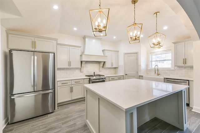 kitchen with sink, appliances with stainless steel finishes, decorative light fixtures, a kitchen island, and custom exhaust hood