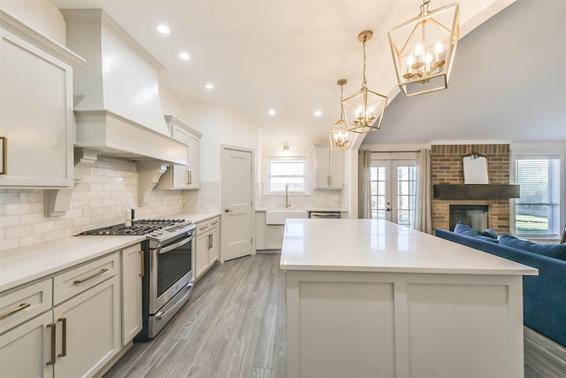 kitchen featuring sink, stainless steel range with gas cooktop, pendant lighting, a fireplace, and custom exhaust hood