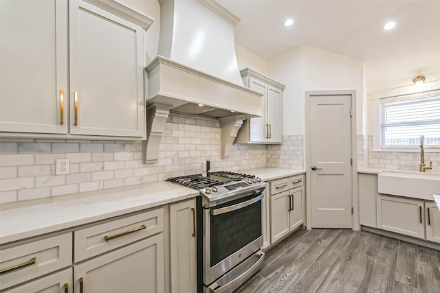 kitchen with dark wood-type flooring, sink, stainless steel gas range, decorative backsplash, and custom range hood