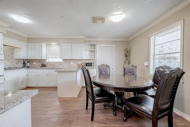 dining space with sink, a wealth of natural light, ornamental molding, and light wood-type flooring