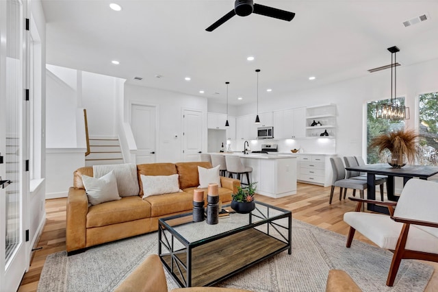 living room featuring ceiling fan with notable chandelier, light hardwood / wood-style flooring, and sink