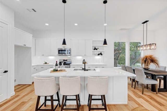 kitchen with stainless steel appliances, sink, white cabinets, light hardwood / wood-style floors, and an island with sink