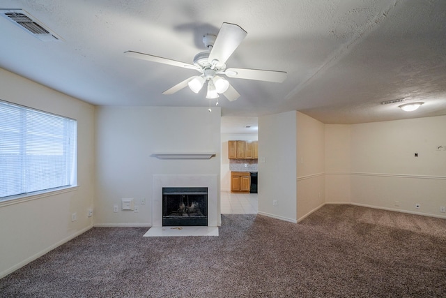 unfurnished living room featuring ceiling fan, light colored carpet, and a textured ceiling