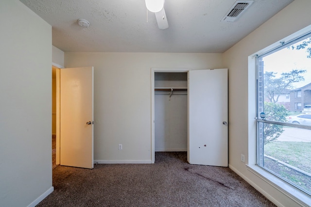 unfurnished bedroom with a closet, dark carpet, multiple windows, and ceiling fan