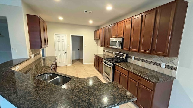 kitchen featuring kitchen peninsula, appliances with stainless steel finishes, backsplash, dark stone counters, and light tile patterned floors