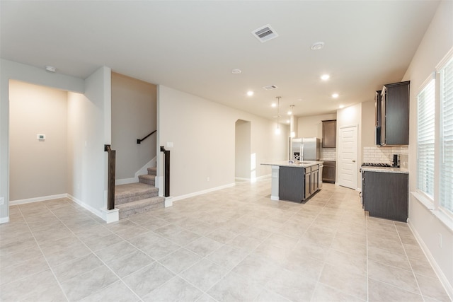 kitchen with tasteful backsplash, light tile patterned floors, decorative light fixtures, stainless steel fridge with ice dispenser, and an island with sink