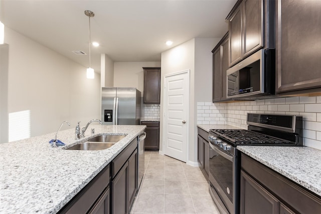 kitchen with sink, hanging light fixtures, stainless steel appliances, light stone counters, and backsplash