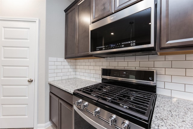 kitchen with dark brown cabinetry, stainless steel appliances, light stone counters, and backsplash