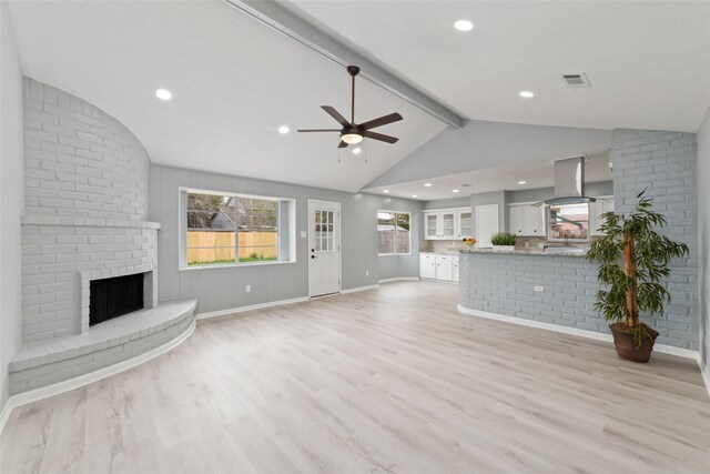 unfurnished living room with vaulted ceiling with beams, light wood-type flooring, a brick fireplace, and ceiling fan