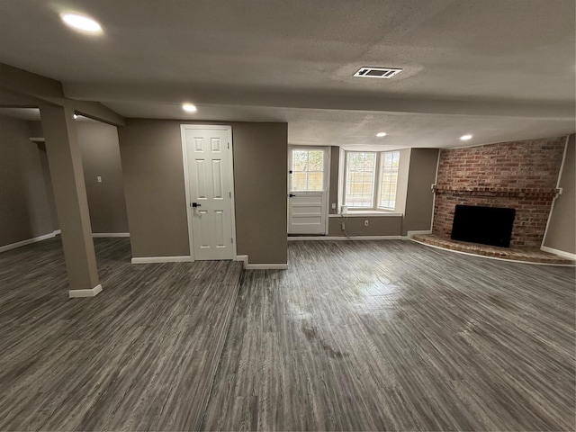 unfurnished living room featuring a textured ceiling, dark hardwood / wood-style flooring, and a brick fireplace