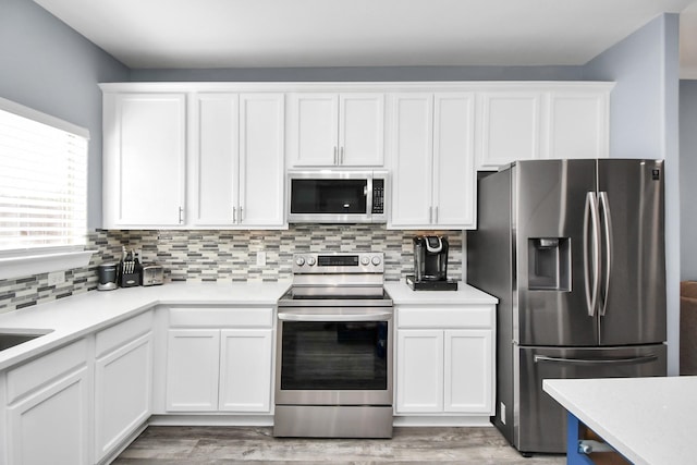 kitchen with tasteful backsplash, white cabinetry, stainless steel appliances, and light wood-type flooring