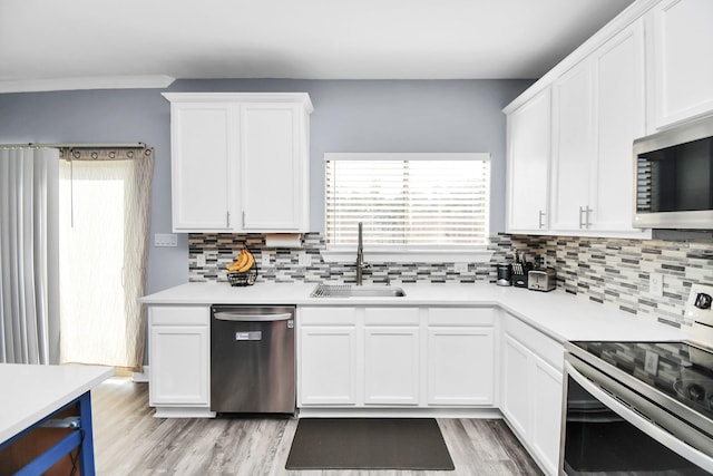 kitchen with white cabinets, sink, light wood-type flooring, tasteful backsplash, and stainless steel appliances