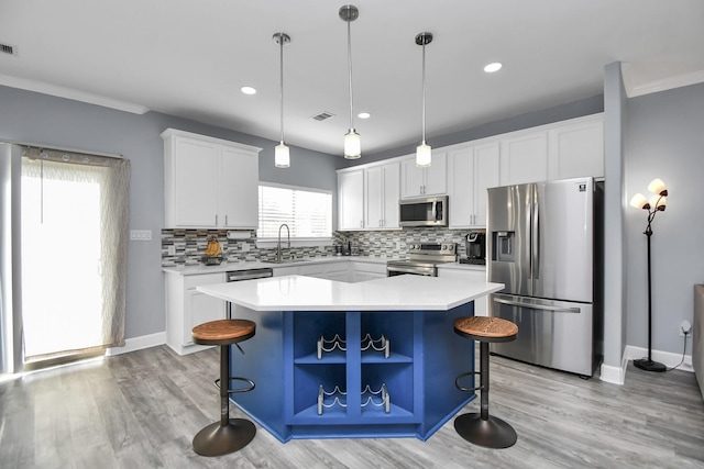 kitchen featuring stainless steel appliances, sink, white cabinetry, a kitchen island, and hanging light fixtures