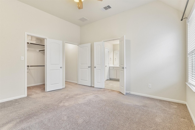 unfurnished bedroom featuring vaulted ceiling, connected bathroom, a walk in closet, ceiling fan, and light carpet