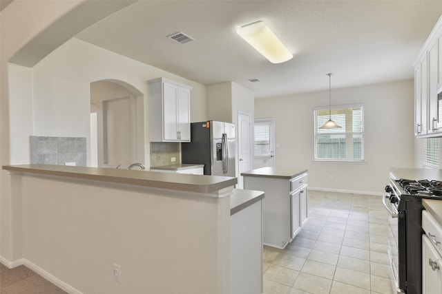 kitchen featuring range, hanging light fixtures, stainless steel fridge, a kitchen island, and white cabinets