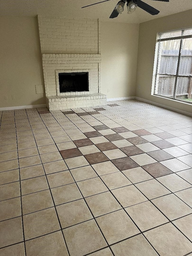 unfurnished living room featuring ceiling fan, a fireplace, light tile patterned floors, and a textured ceiling