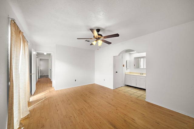 unfurnished bedroom with ceiling fan, light hardwood / wood-style floors, a textured ceiling, and ensuite bath