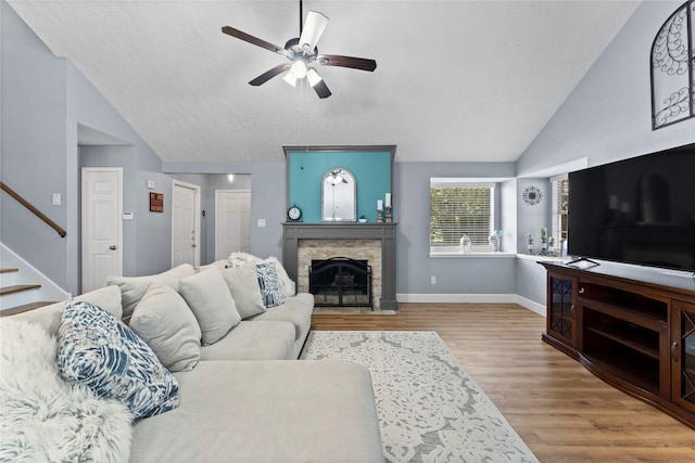 living room featuring a textured ceiling, vaulted ceiling, ceiling fan, light hardwood / wood-style flooring, and a fireplace