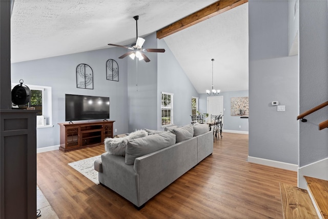 living room featuring beamed ceiling, ceiling fan with notable chandelier, a healthy amount of sunlight, and wood-type flooring