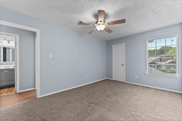 unfurnished bedroom featuring ensuite bath, ceiling fan, carpet floors, and a textured ceiling