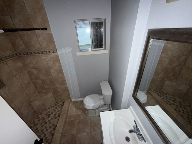 bathroom with tile patterned flooring, vanity, toilet, and tiled shower