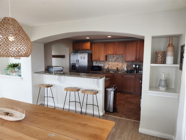 22901 Buena St, Galveston, TX 77554 - kitchen featuring backsplash, dark stone countertops, stainless steel fridge, wood-type flooring, and a breakfast bar