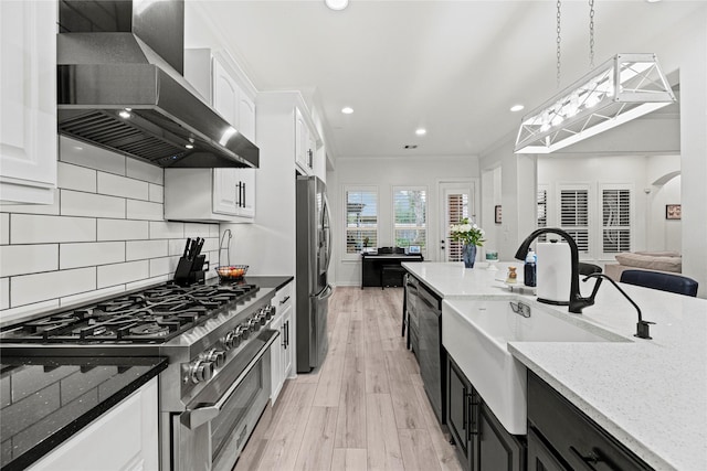 kitchen featuring pendant lighting, wall chimney range hood, white cabinetry, and appliances with stainless steel finishes