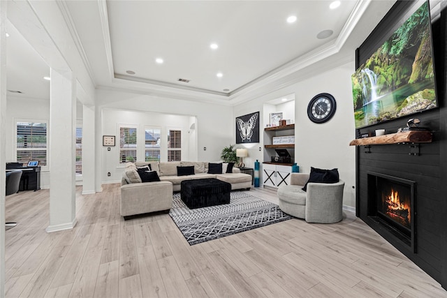 living room with a tray ceiling, a fireplace, light hardwood / wood-style flooring, and plenty of natural light