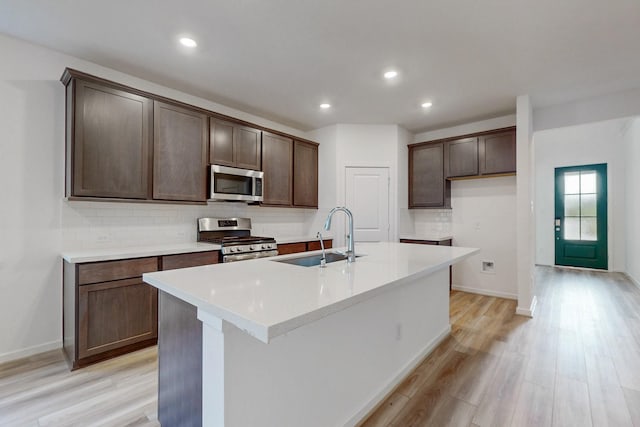 kitchen featuring a center island with sink, sink, light wood-type flooring, dark brown cabinetry, and stainless steel appliances